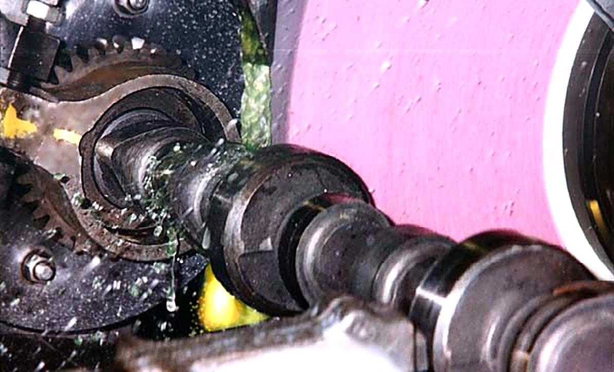 A camshaft being ground, with coolant spraying off the grinding wheel